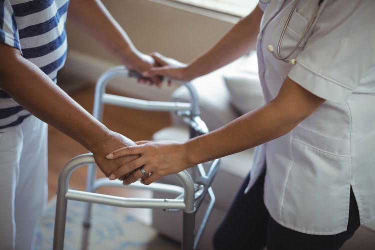 Mid section of female doctor helping senior woman to walk with walker at home